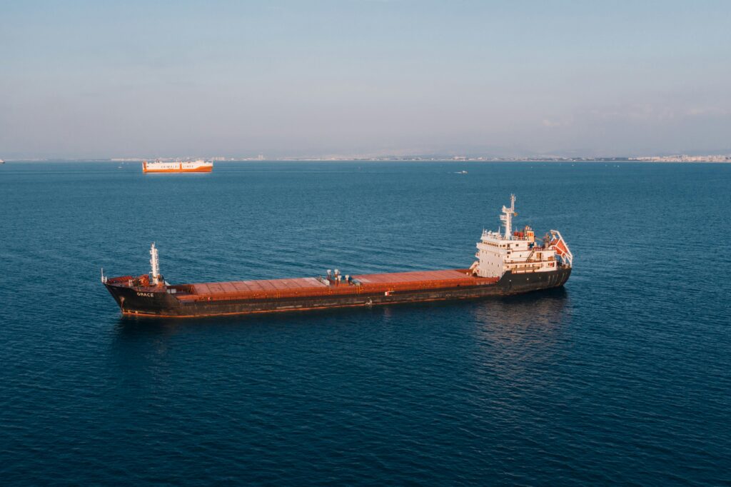 Aerial view of a cargo ship sailing in the open sea under clear skies, showcasing maritime transport.