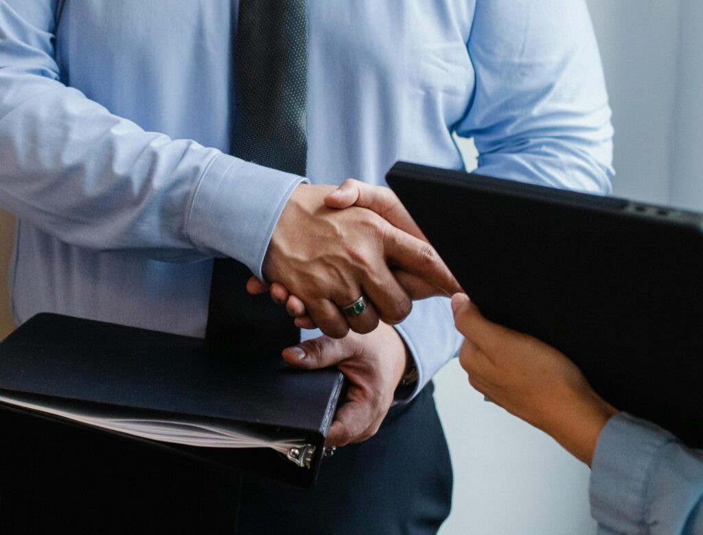 Business handshake between colleagues in a formal office meeting setting.